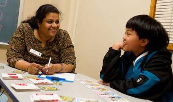 teacher sits at low table with child.  activity materials scattered on table, they're both smiling